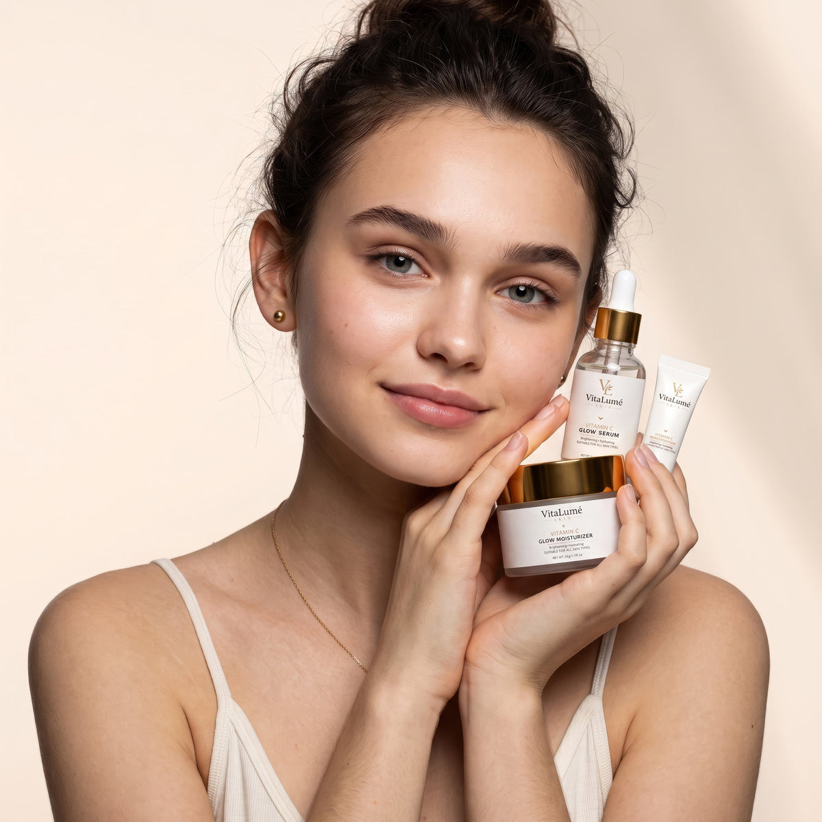 Eye cream skincare set with clear serum dropper, white tube and jar with gold accents held beside a woman's face